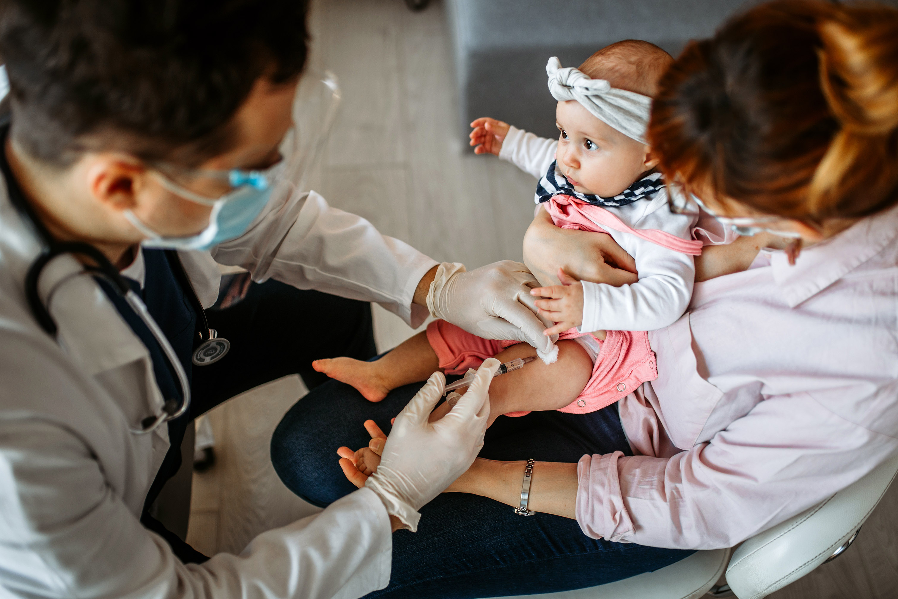 Una mujer que sostiene a su bebé que está recibiendo una vacuna de un médico