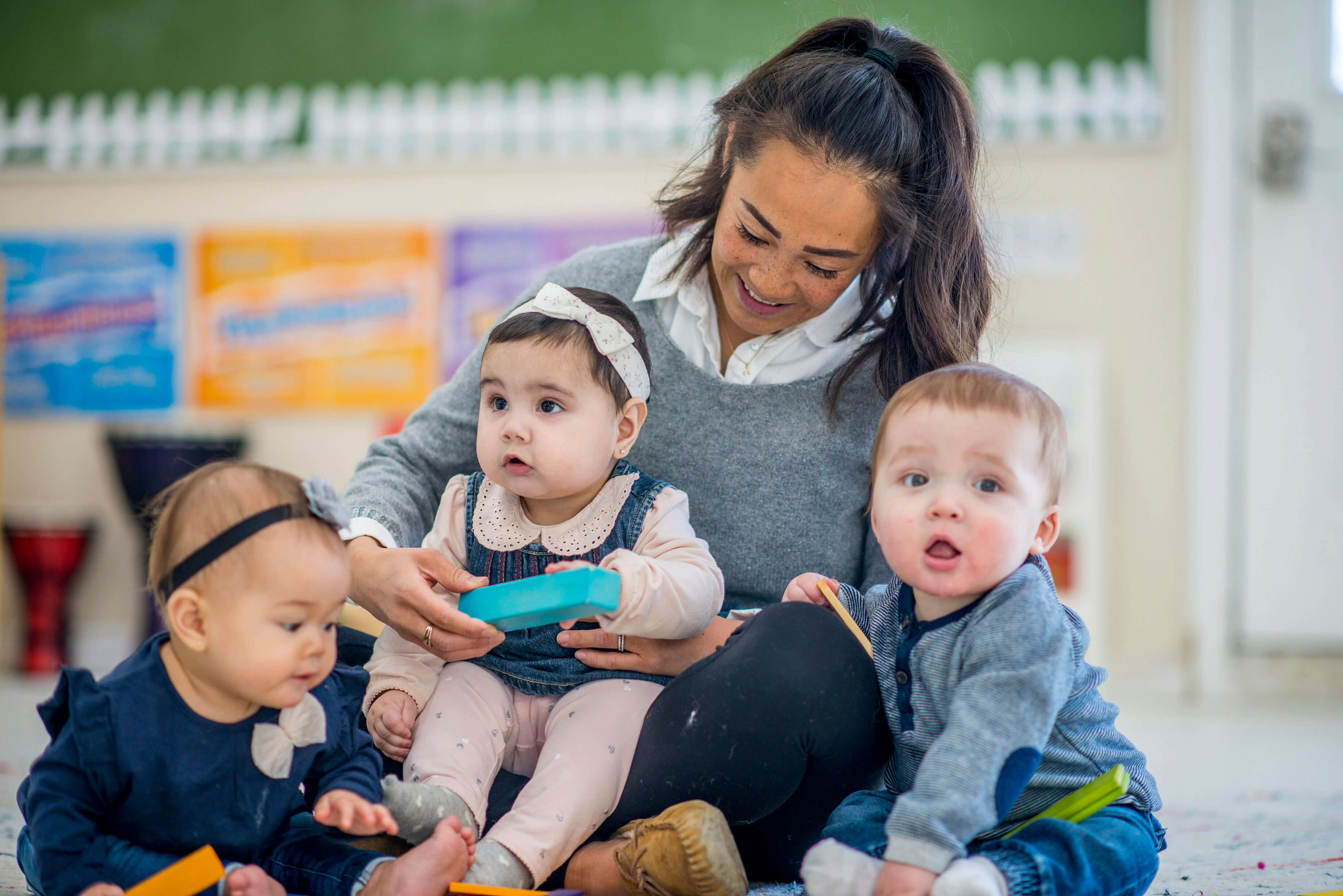 Child care provider sitting on the floor with three children playing with toys