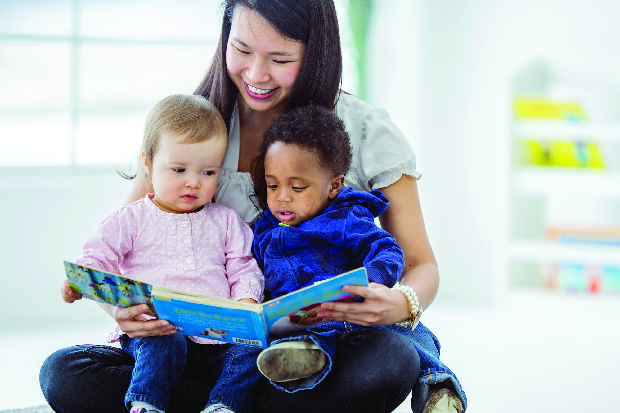 Proveedor de cuidado infantil sentado en el suelo leyendo a dos niños