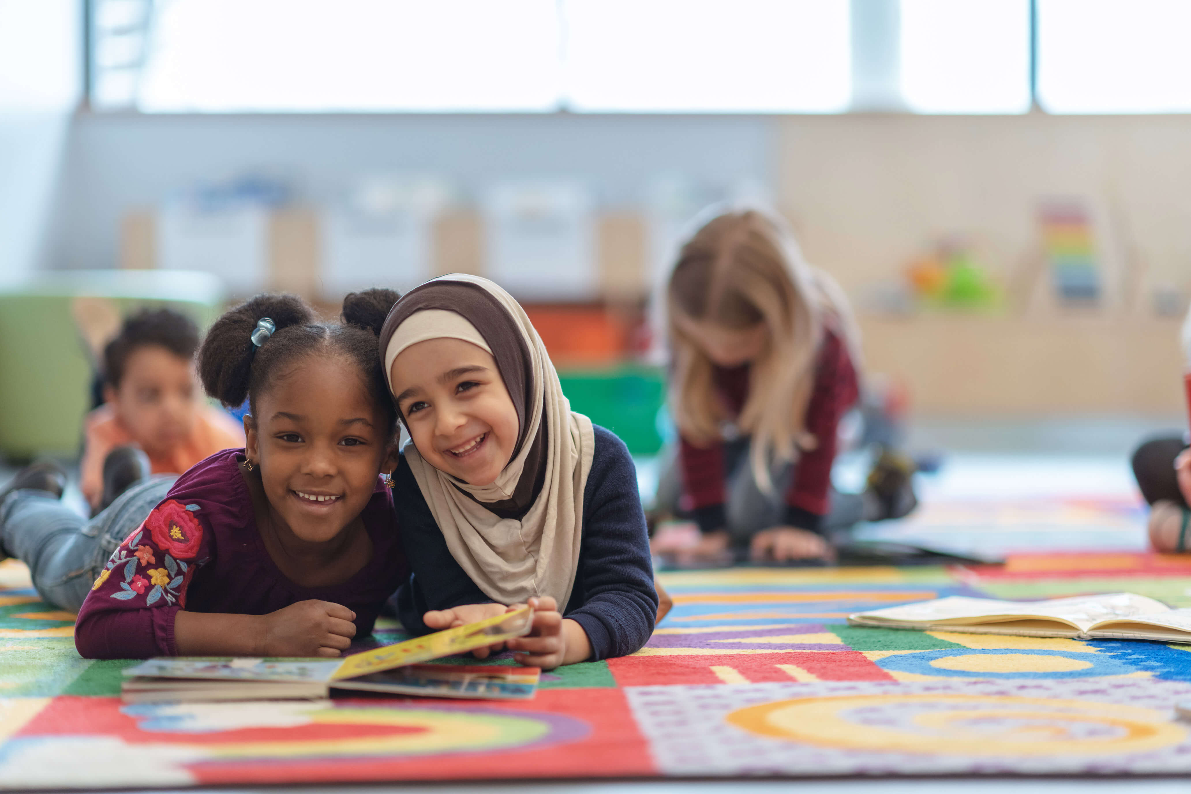 Dos niños en edad preescolar tendidos en el suelo leyendo un libro