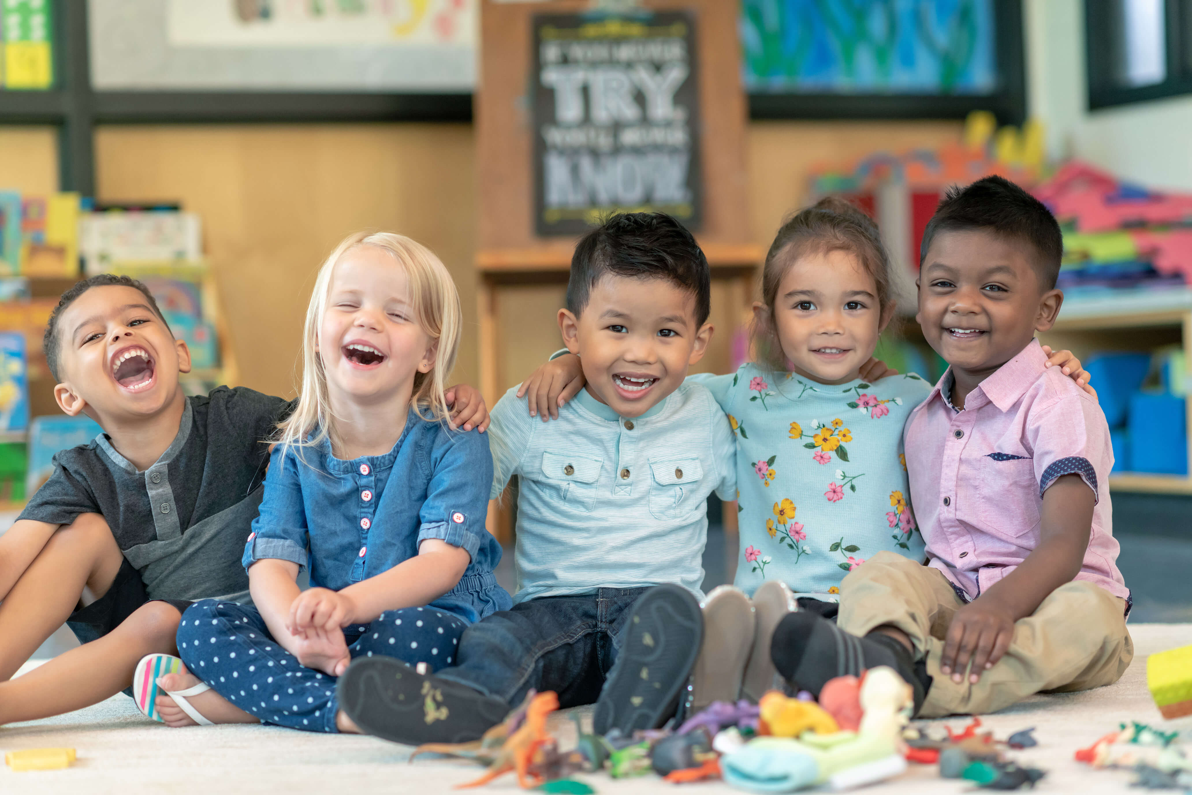 Five children sitting on the floor smiling and playing with toys