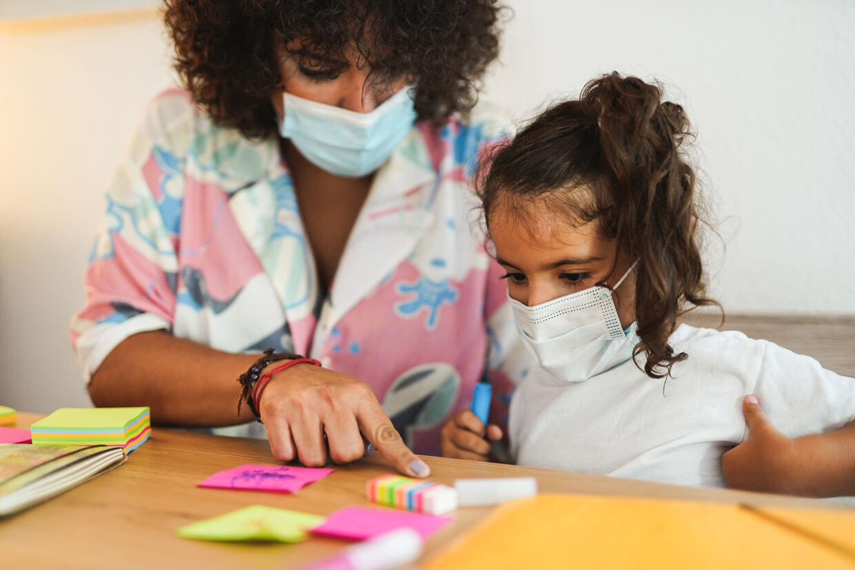 Teacher helping student with school work while wearing masks