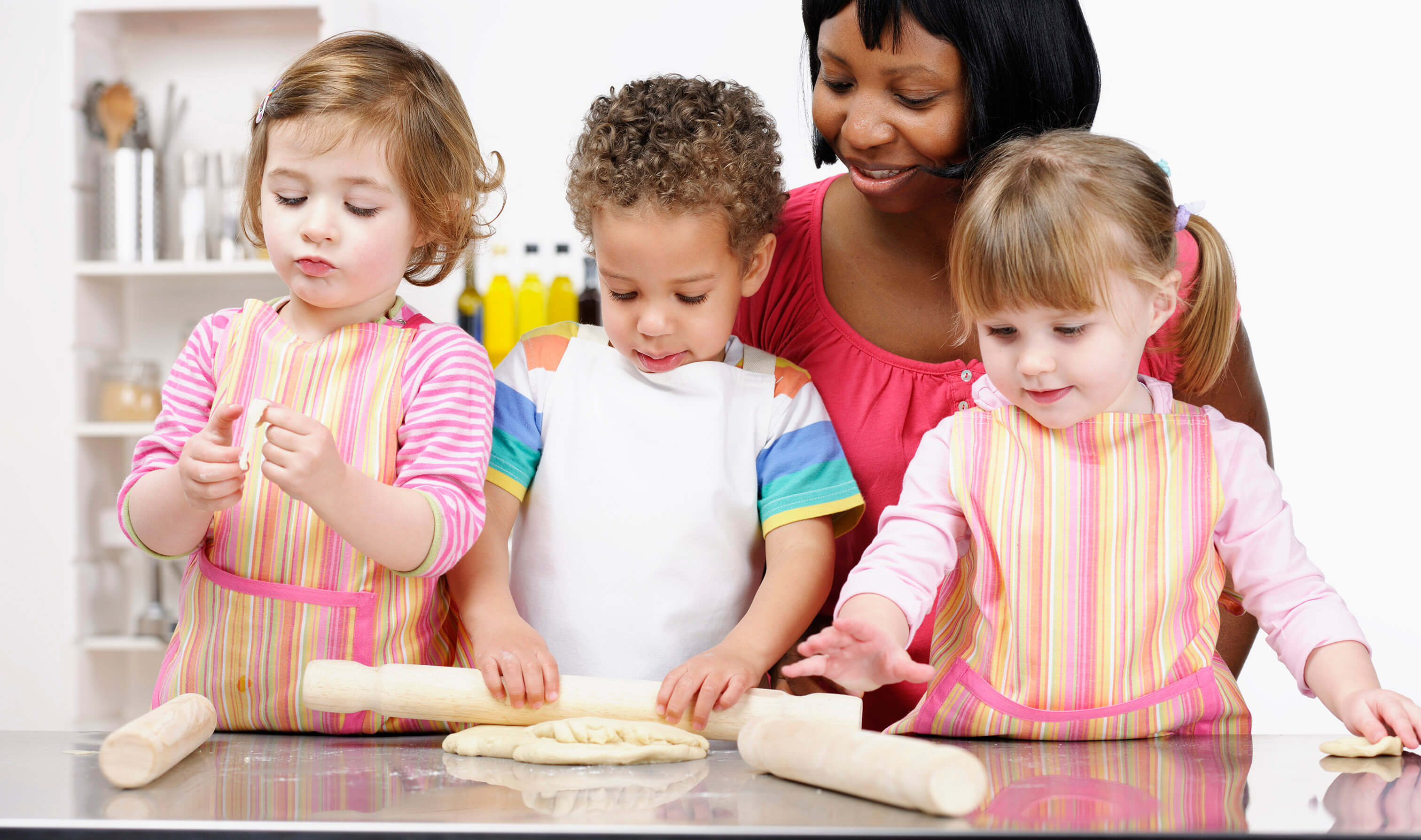 Child care provider helping three children roll dough