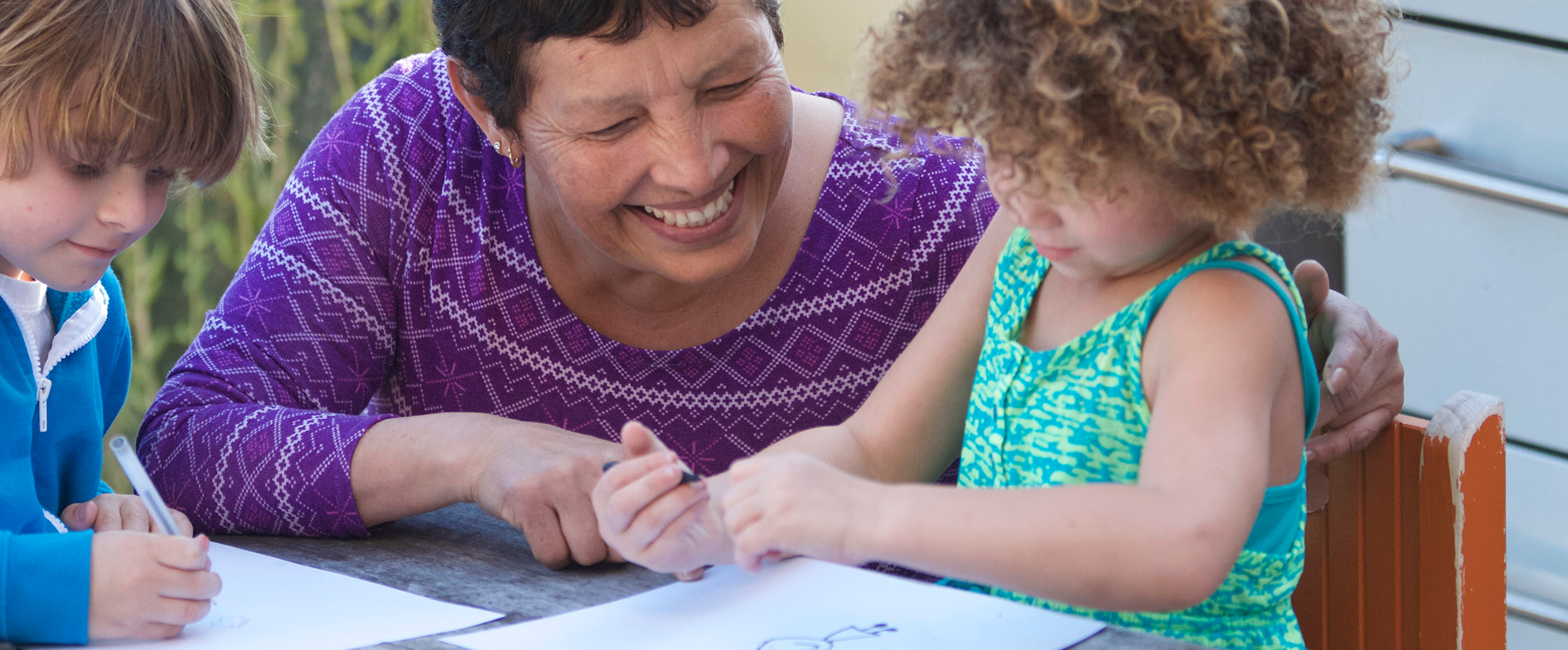Una proveedora de cuidado infantil ayuda a dos niños con sus obras de arte.