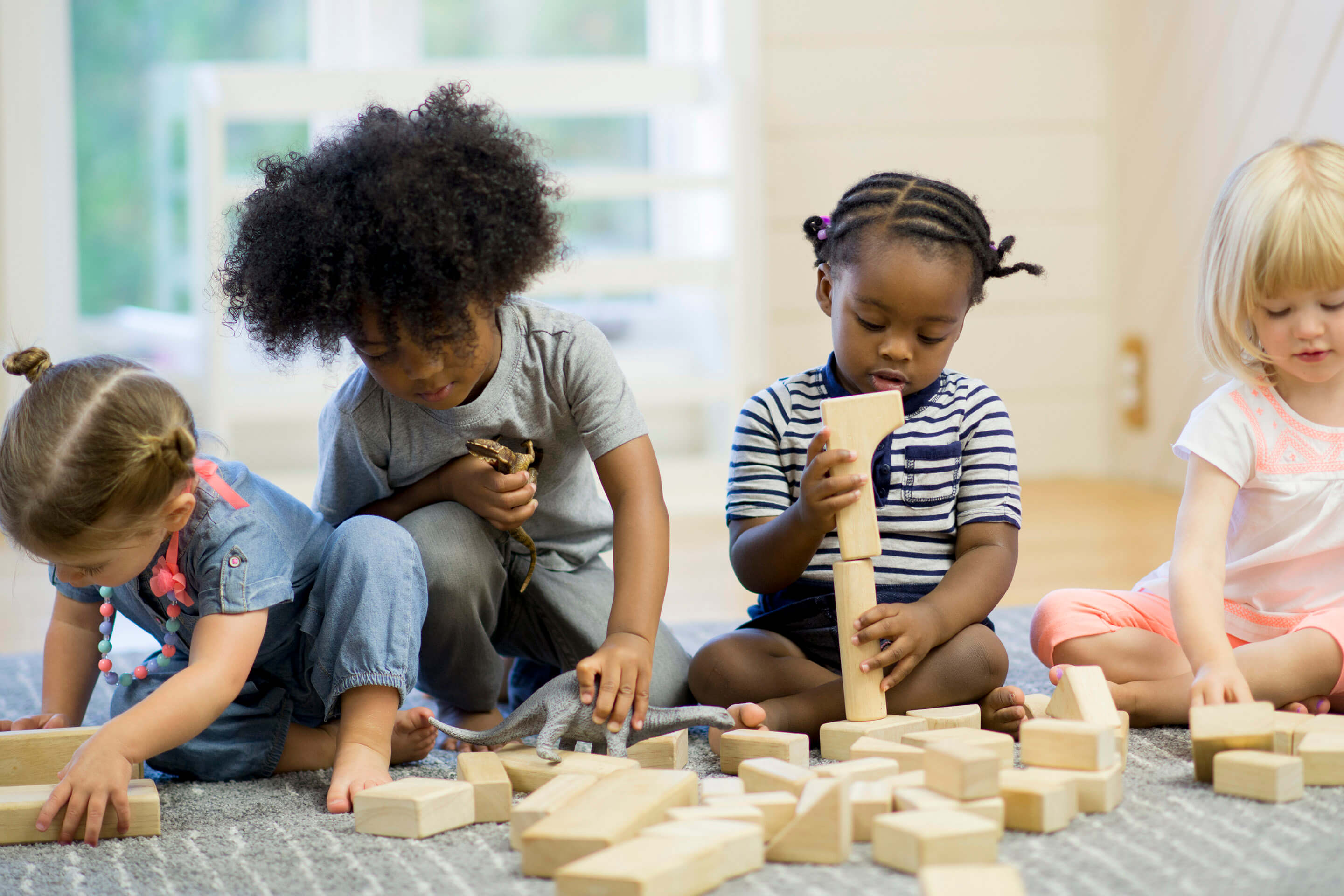 Four toddlers playing on the floor with blocks