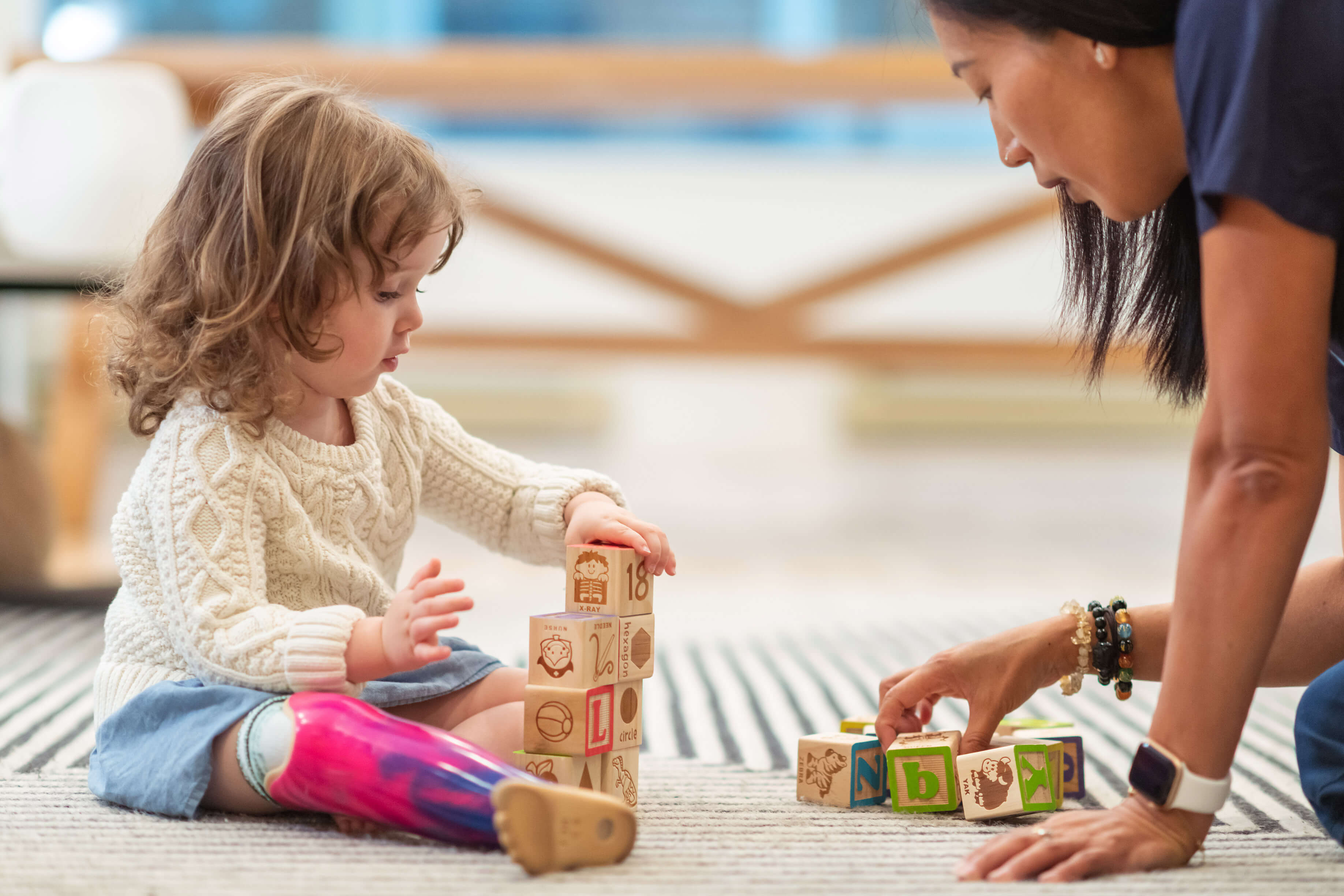 Toddler sitting on the floor playing blocks with child care provider