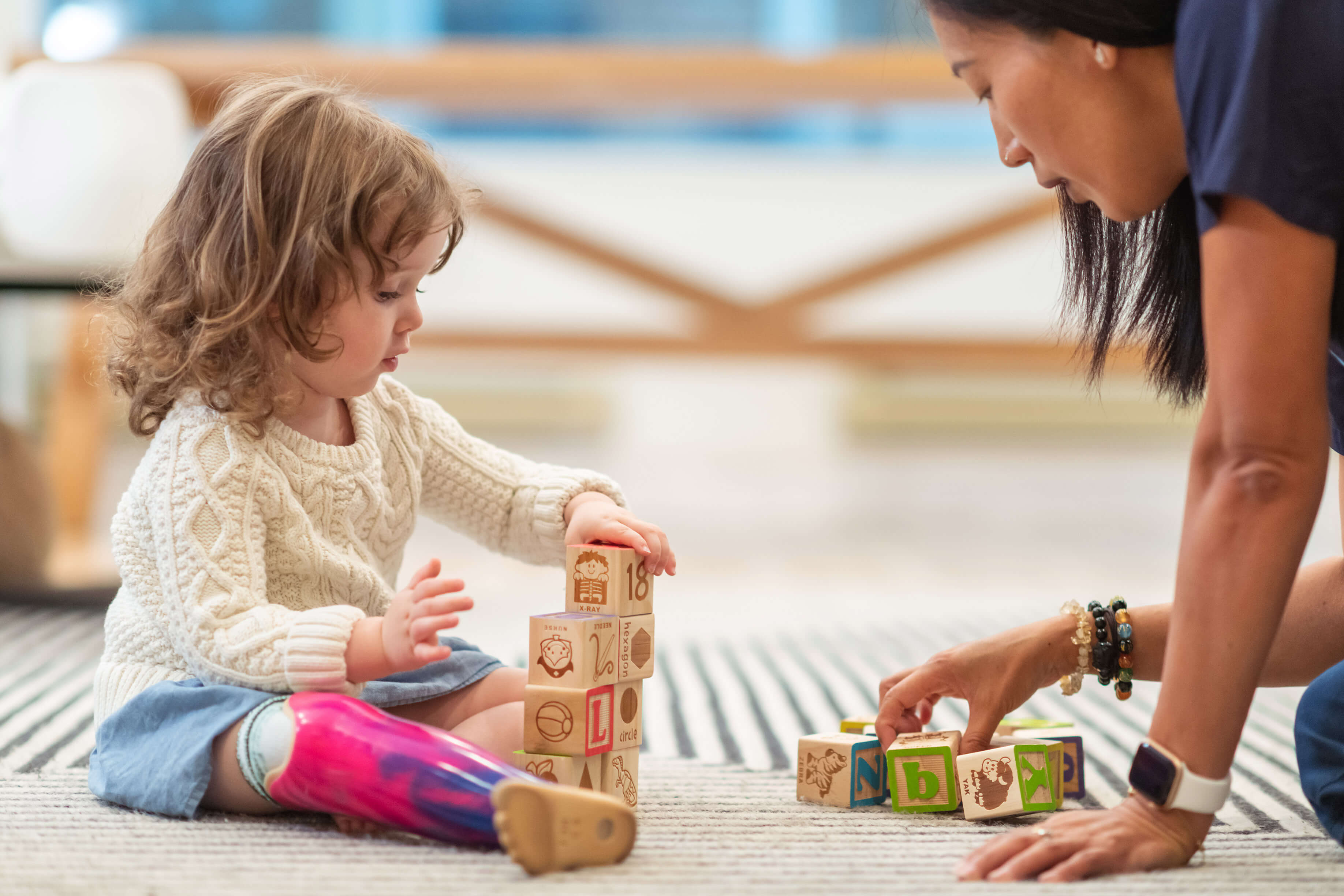 A child sitting on the floor playing with her child care provider